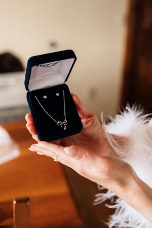 Hands holding an open jewelry box with a delicate bow necklace and stud earrings set on velvet.