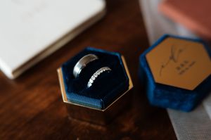 Elegant wedding bands displayed in a blue velvet hexagonal ring box on wooden surface.