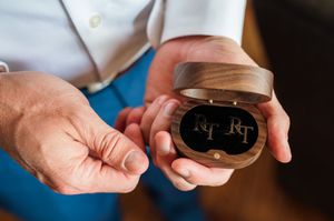 Groom holds wooden ring box with engraved monogram initials on black velvet interior closeup.