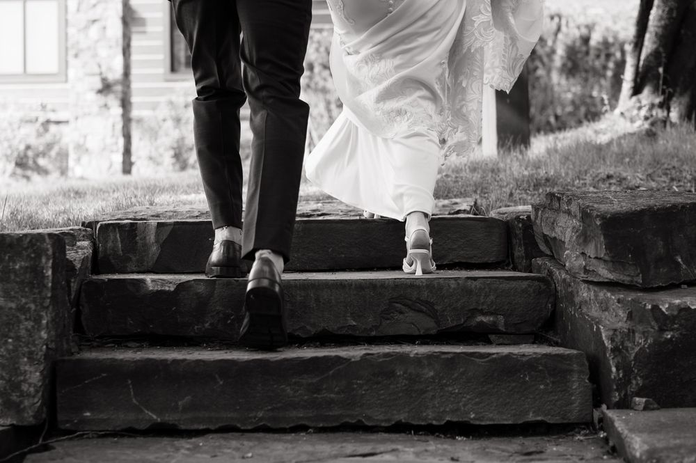 Black and white photo of bride and groom walking up stone steps, showing their shoes and wedding attire.
