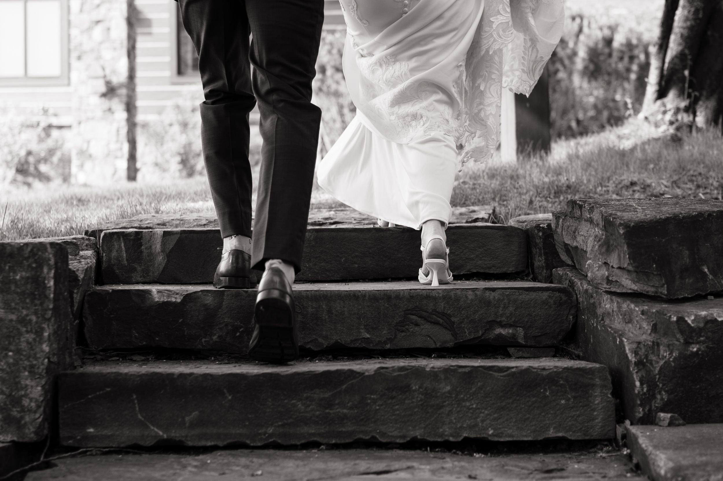 Black and white photo of bride and groom walking up stone steps, showing their shoes and wedding attire.