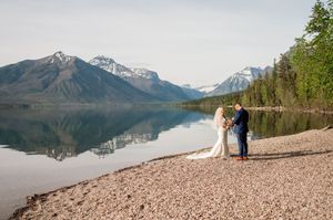 Couple exchanging vows on rocky lakeshore with stunning mountain reflections at Glacier National Park wedding.