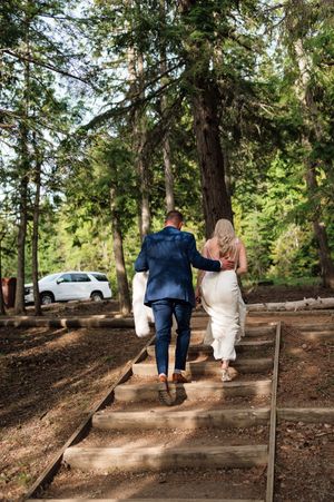 Bride and groom walking up wooden steps through sunlit forest after wedding ceremony.
