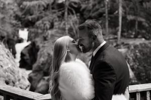 Black and white photo of bride and groom sharing intimate moment near waterfall on wooden bridge.