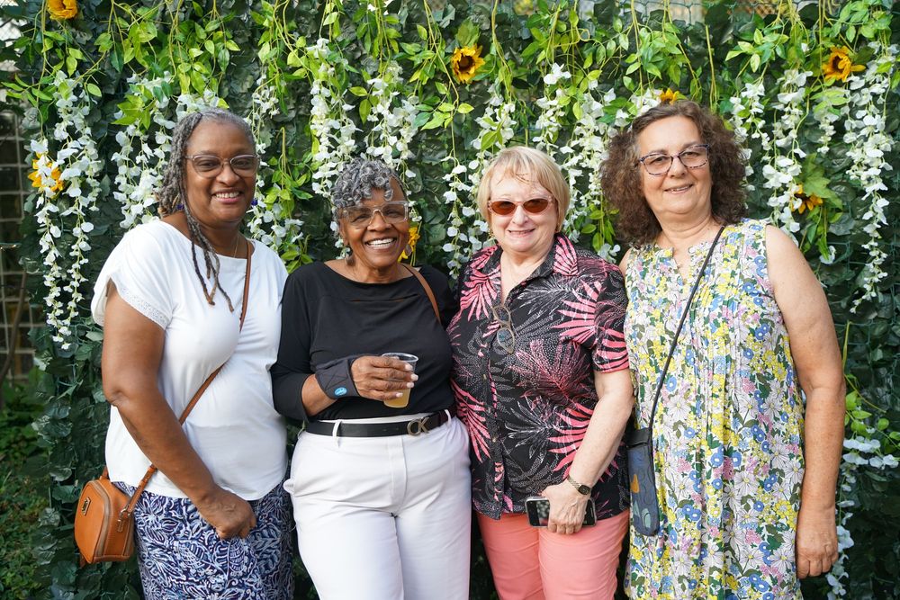 Four women pose together smiling in front of a floral wall.