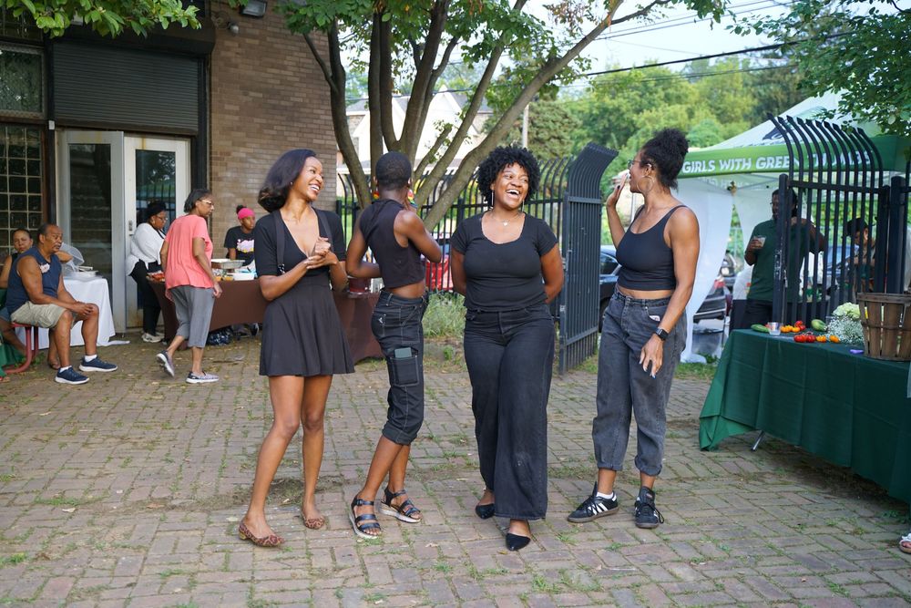Three women socializing outdoors at a community gathering event in an urban garden setting.