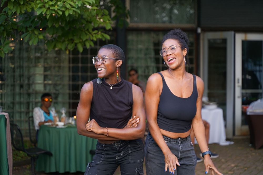 Two women in black crop tops smiling and laughing together at an outdoor event.