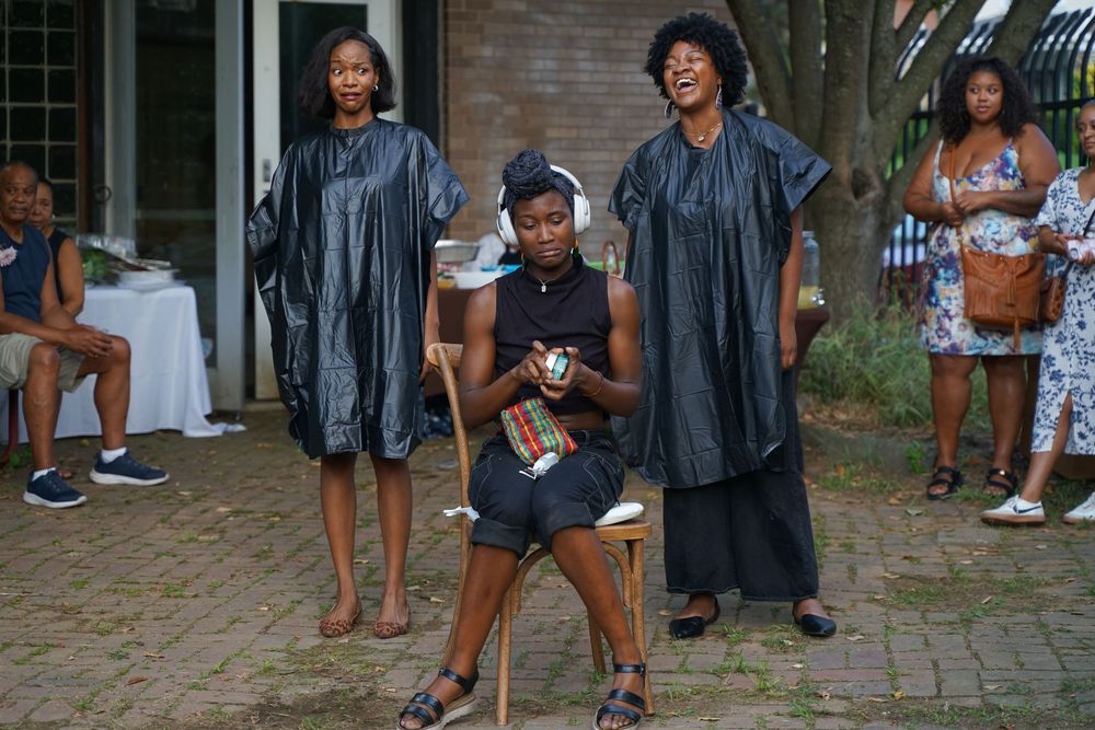 Three women in black attire stand outdoors at a garden event.