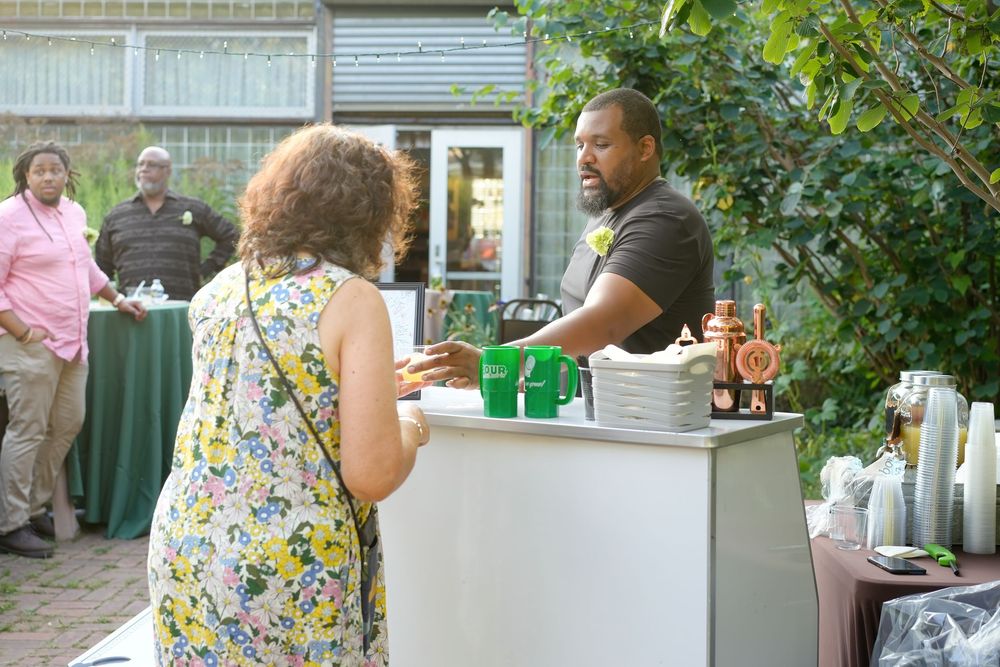 Man serves drinks at an outdoor bar during a garden party.