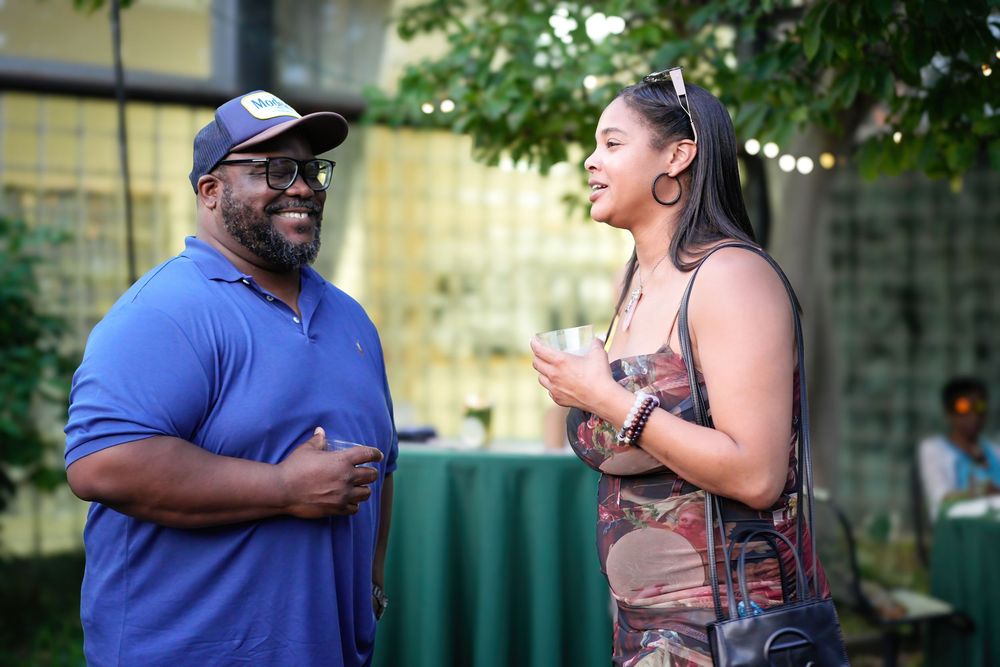 A man and woman laughing and conversing outdoors at a social gathering event.