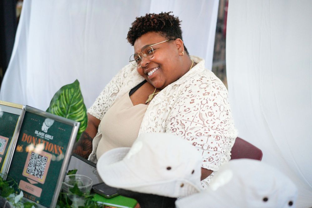 A smiling woman sitting at a vendor table with plants and a QR code sign display.