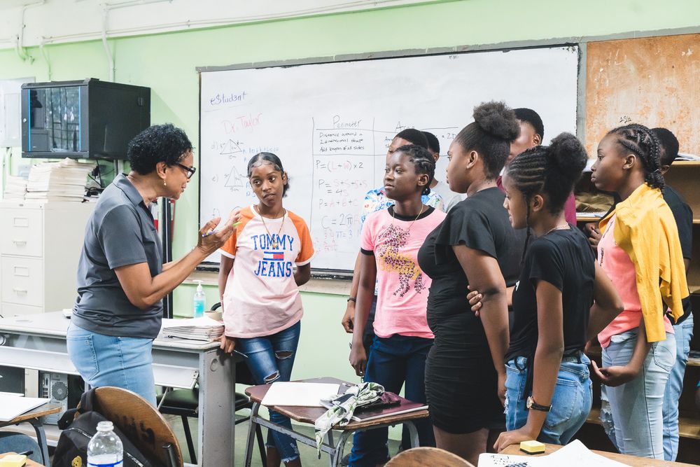 Teacher speaking with group of young Black students standing in classroom.