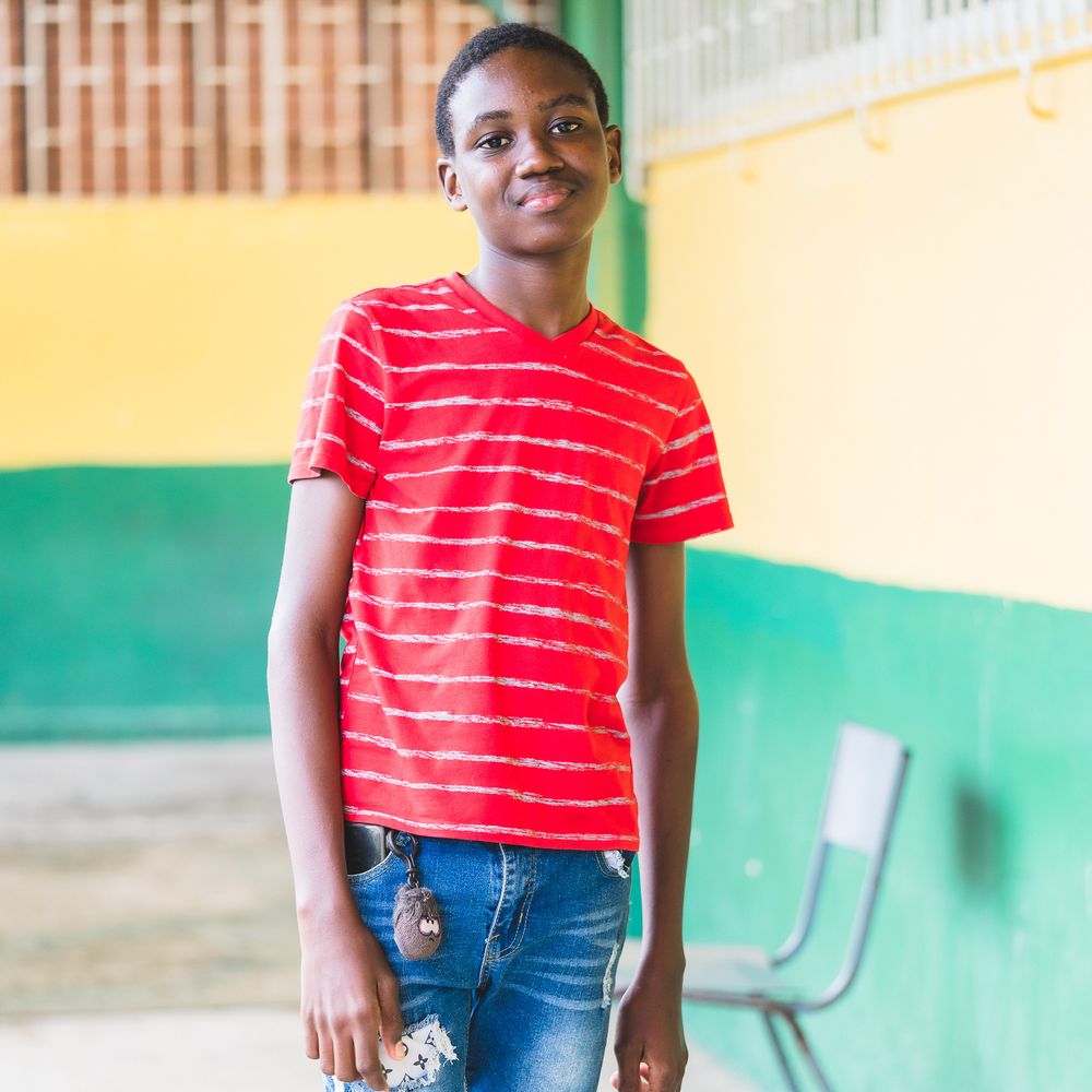 Smiling young African boy in a red striped t-shirt standing outdoors at a colorful school.