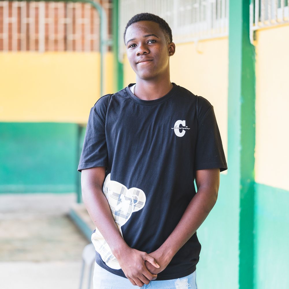 Young Black teenage boy in black graphic t-shirt smiling outdoors at school.