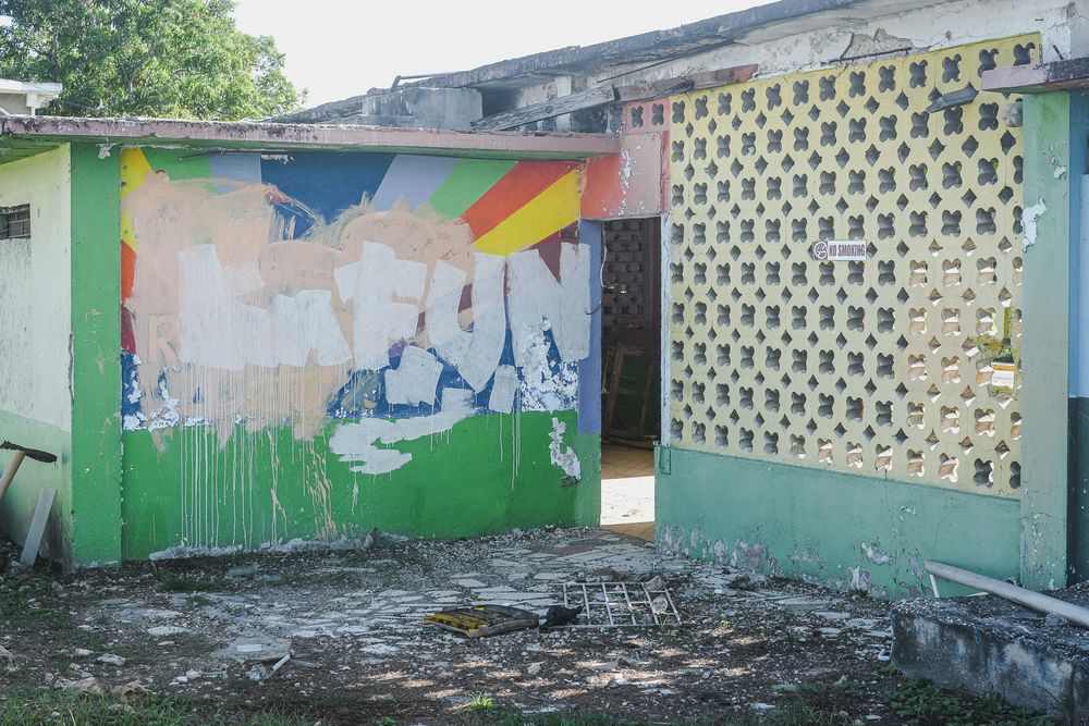 Abandoned building with peeling colorful murals and decorative concrete block wall outdoors.