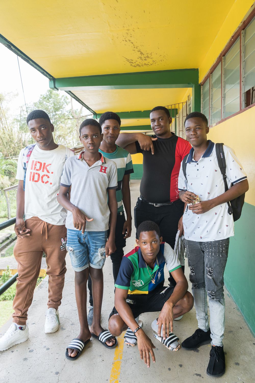 Group of seven young Black men posing together on a colorful yellow and green school corridor.