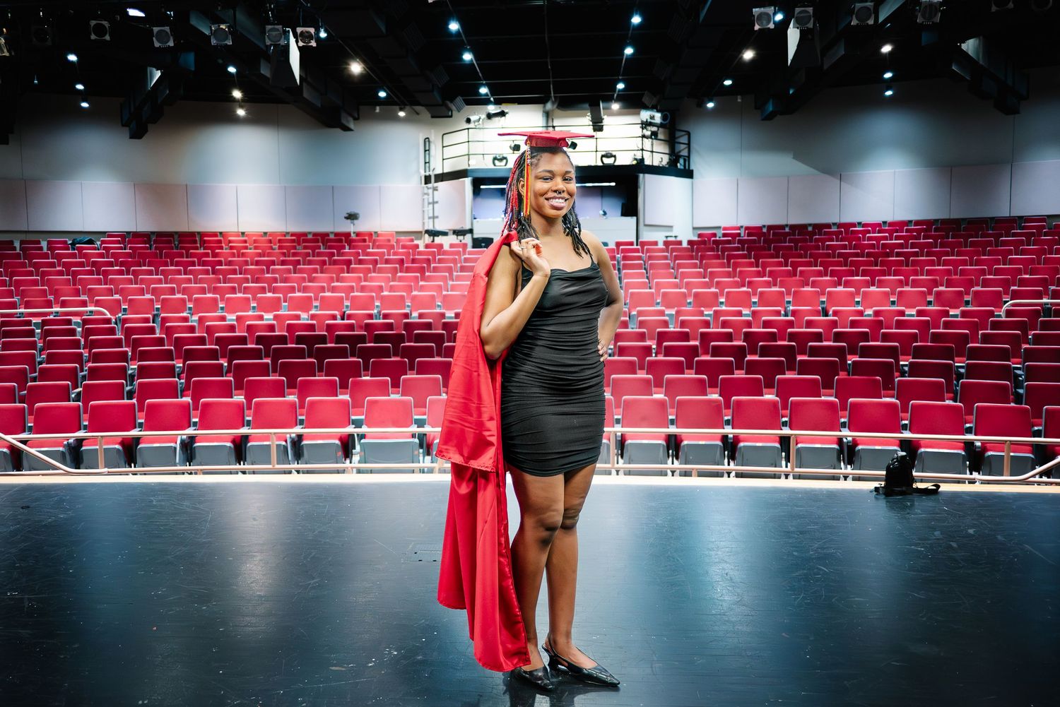 High school theater graduate standing on stage in red graduation cap and gown during Washington senior portrait session