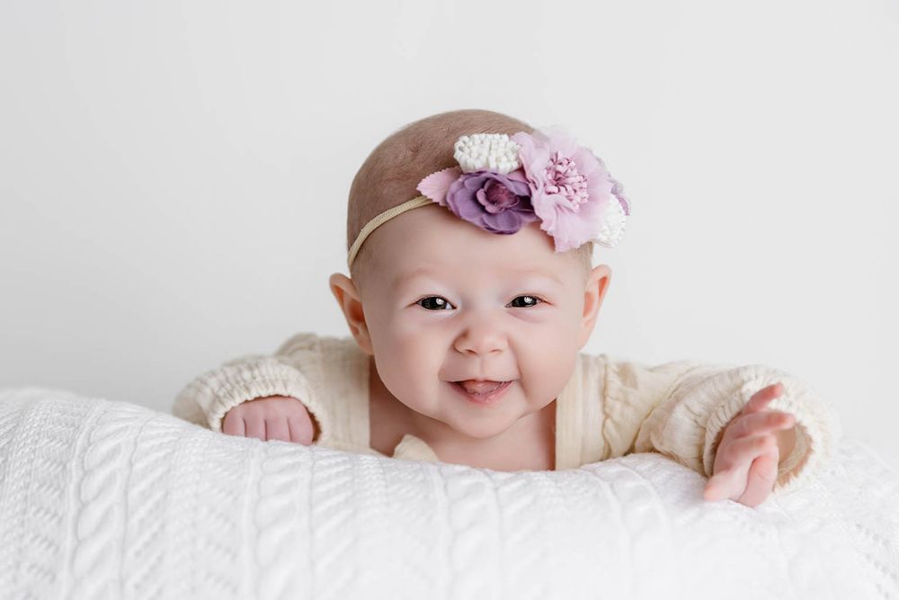 Smiling baby girl in cream knit outfit wearing purple floral headband by Winchester two month old baby photographer.