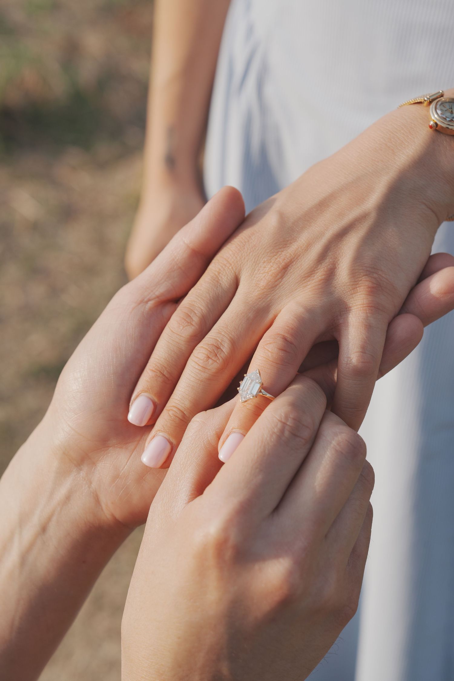 Close-up of a marriage proposal with a diamond engagement ring being placed on a woman's finger outdoors.
