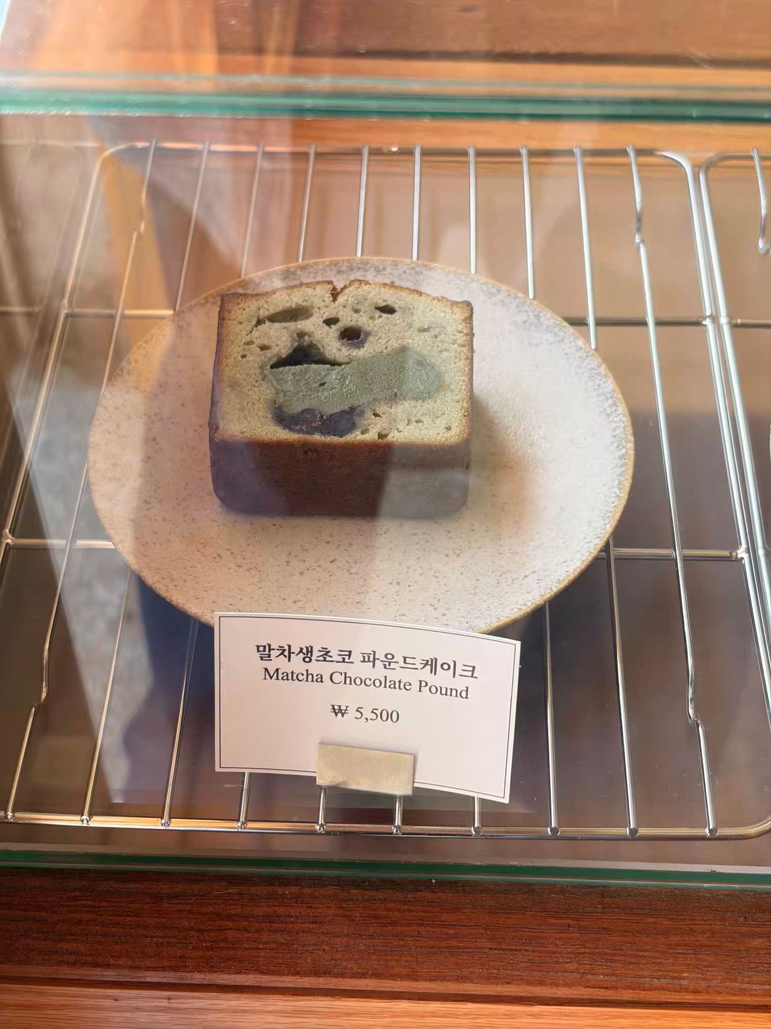 A slice of matcha chocolate pound cake on a ceramic plate displayed in a glass case, priced at ₩5,500.