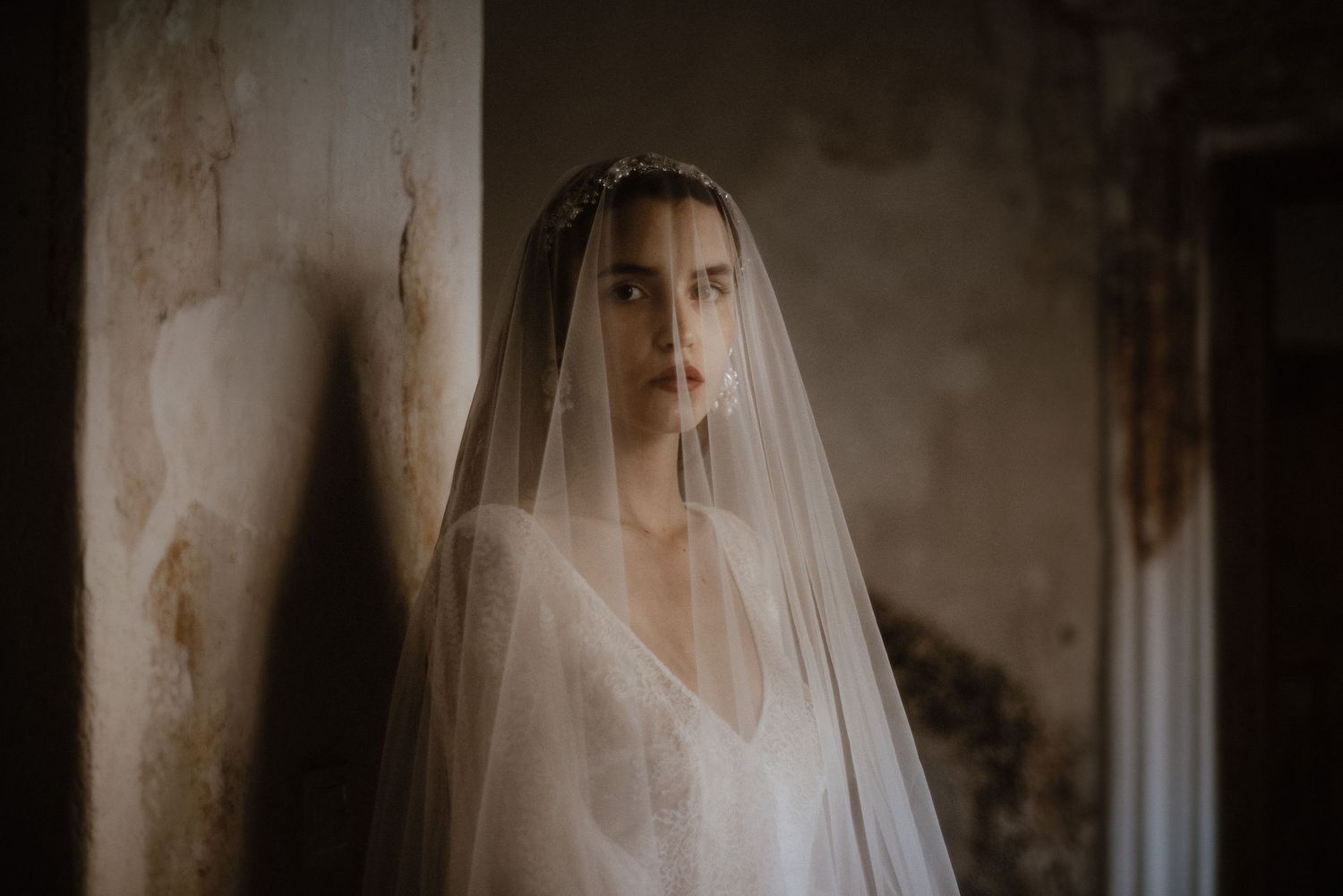 Bride in strapless white ballgown with veil poses oceanside, showcasing elegant draped tulle train.