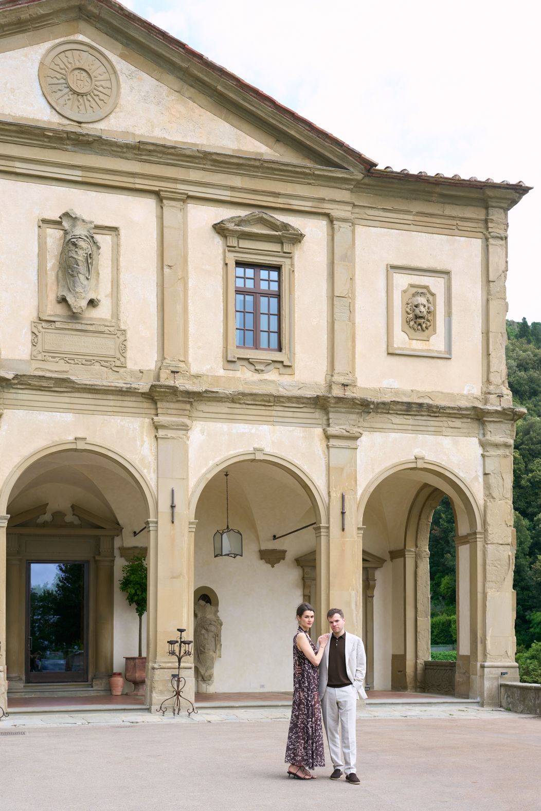 Couple posing in front of an elegant Italian villa with arched colonnades and classical architectural details.