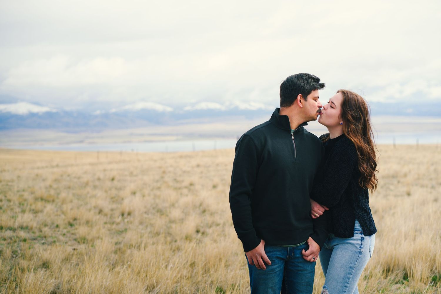 Young couple sharing a romantic kiss while holding hands in a wide open prairie landscape.