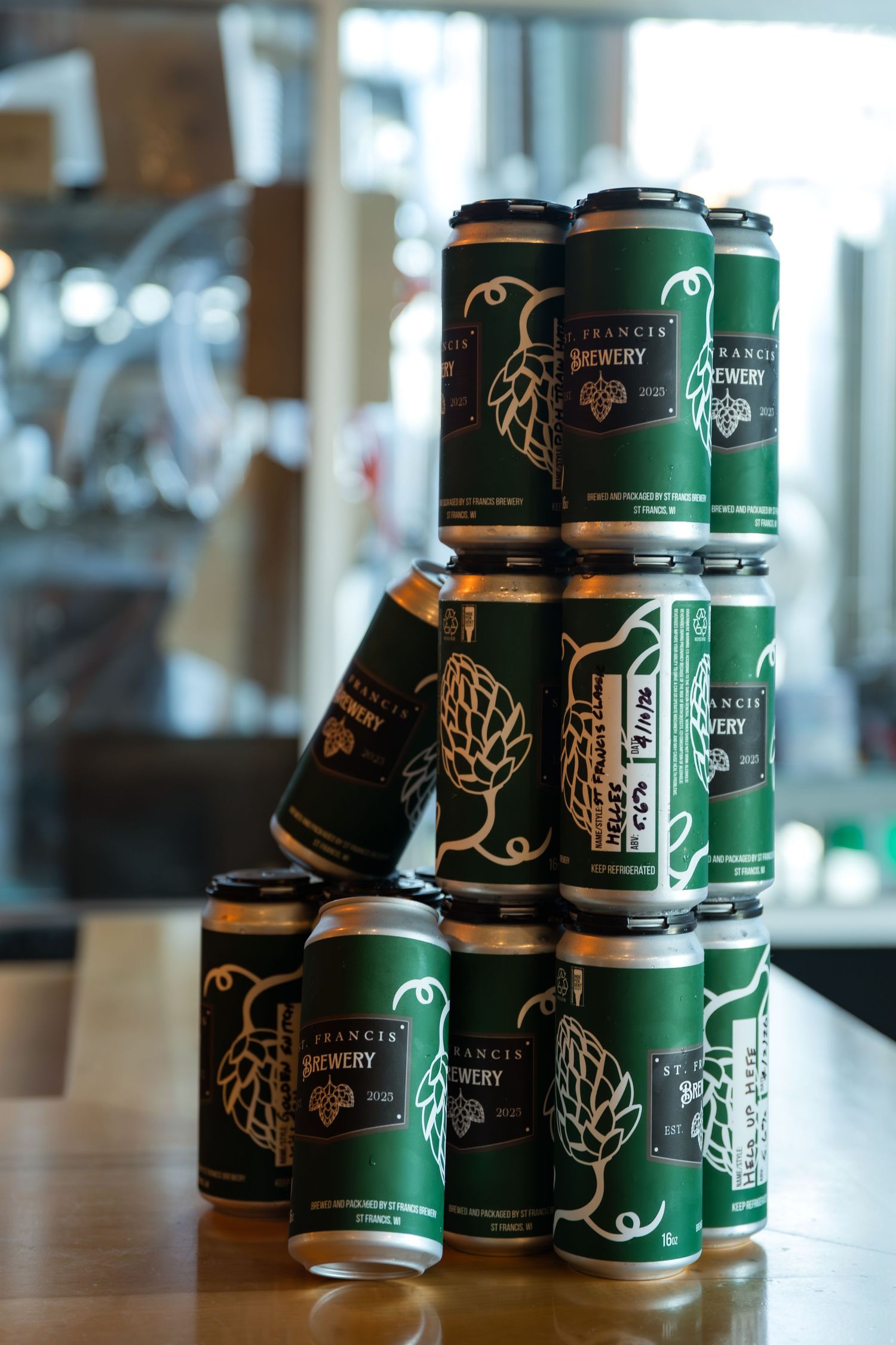 Stack of Francis Brewery green and gold craft beer cans arranged in a pyramid on a wooden bar counter.