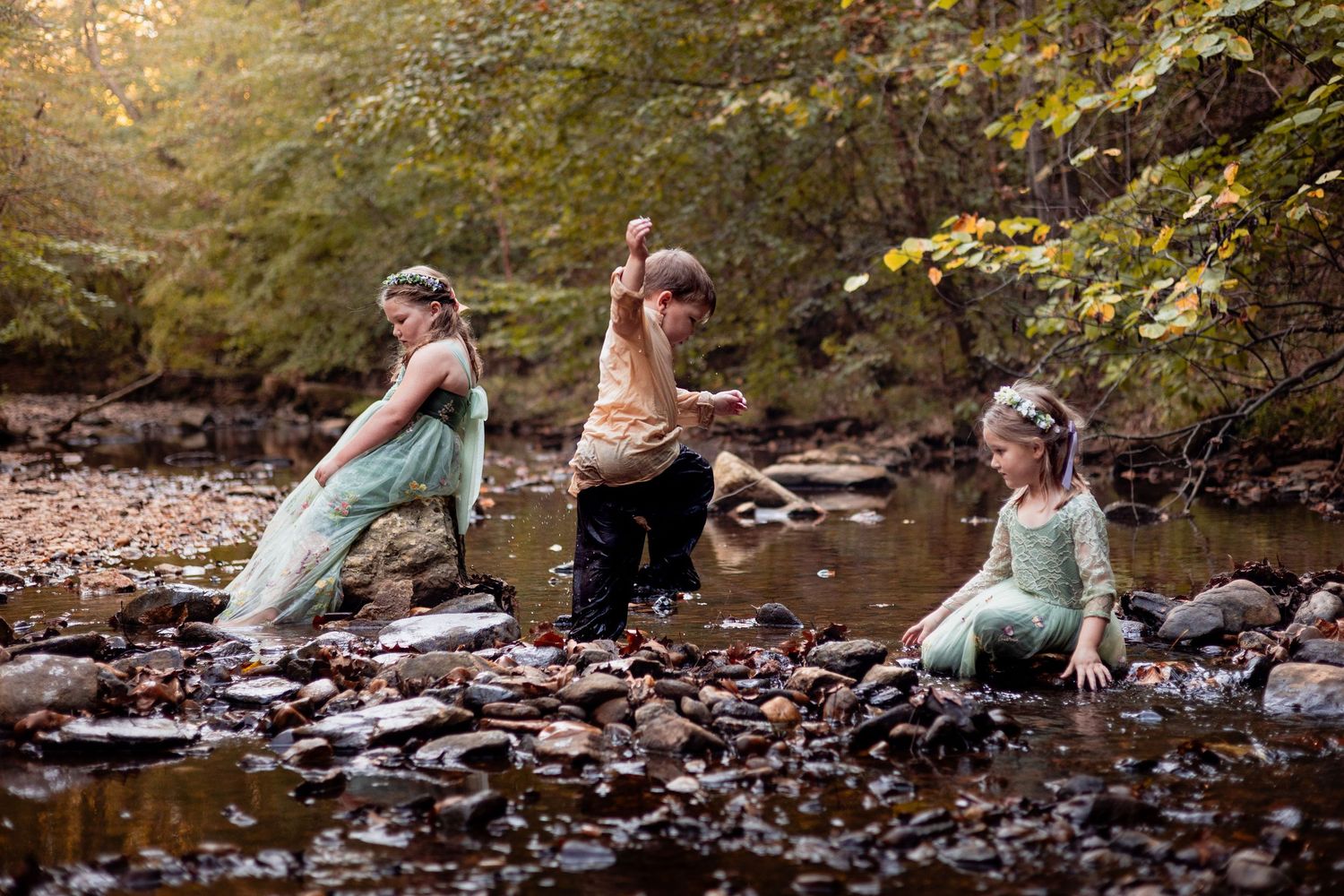 3 children playing in a creek in whimsical clothes.