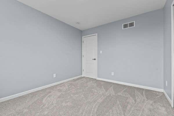 Empty bedroom with light gray walls, neutral carpet, and a single white door.