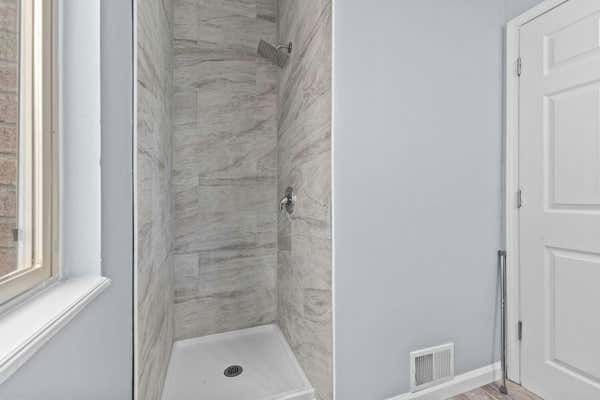 Walk-in shower with marble-style tile surround and white shower base next to a window.