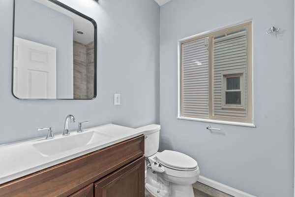 Bathroom with wood vanity, white sink, toilet, and window with shutters.