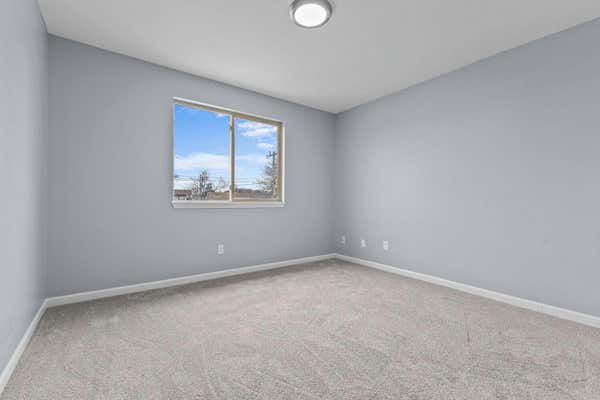 Bright empty bedroom with light gray walls, neutral carpet, and a single window.
