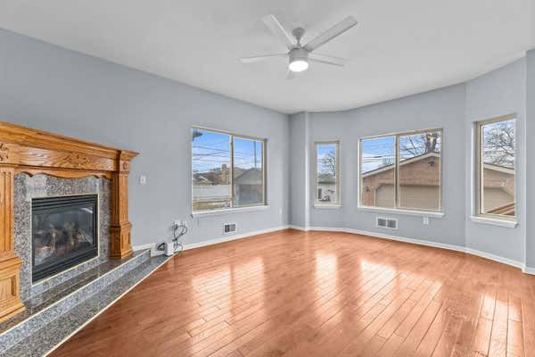 Spacious living room with hardwood floors, gas fireplace, ceiling fan, and large windows.
