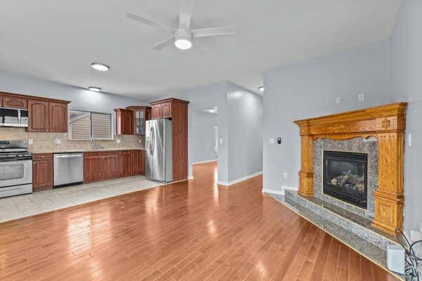 Open kitchen and living area with wood cabinets, stainless appliances, hardwood floors, and fireplace.