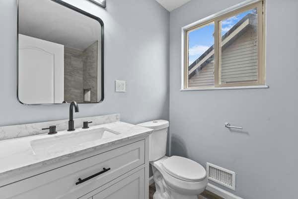 Bathroom with white vanity, marble countertop, toilet, and window with natural light.