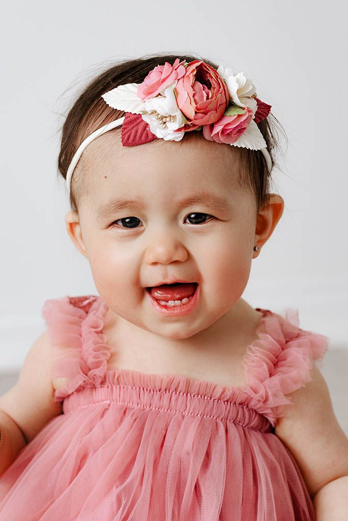 Smiling baby girl in pink tulle dress and floral headband with roses.