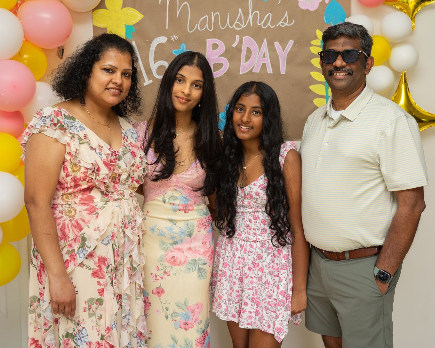 Family of four smiling together at Marisha's birthday party with colorful balloon decorations.