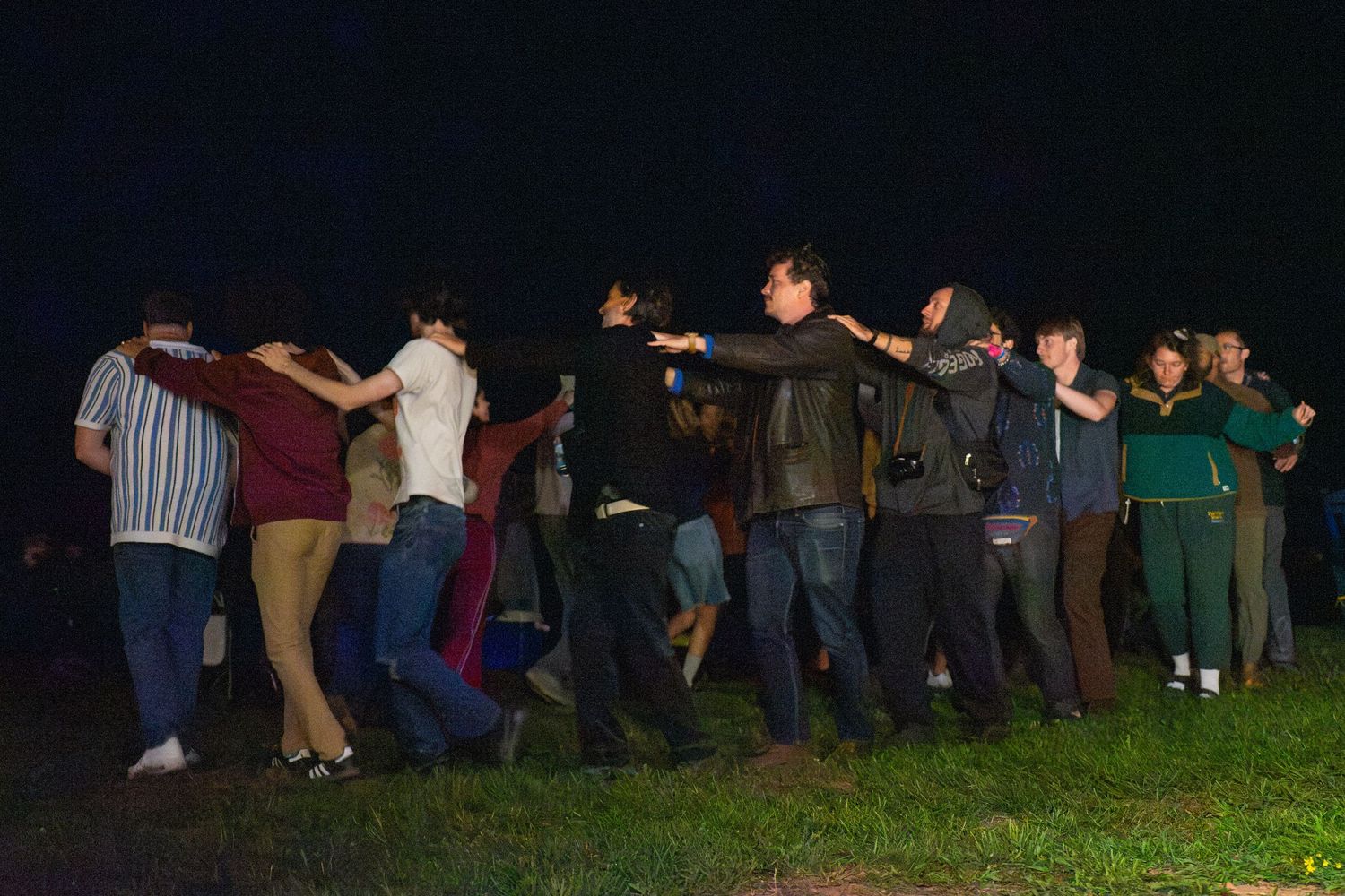 Group of people standing in a line outdoors at night on a grassy field during a social gathering.