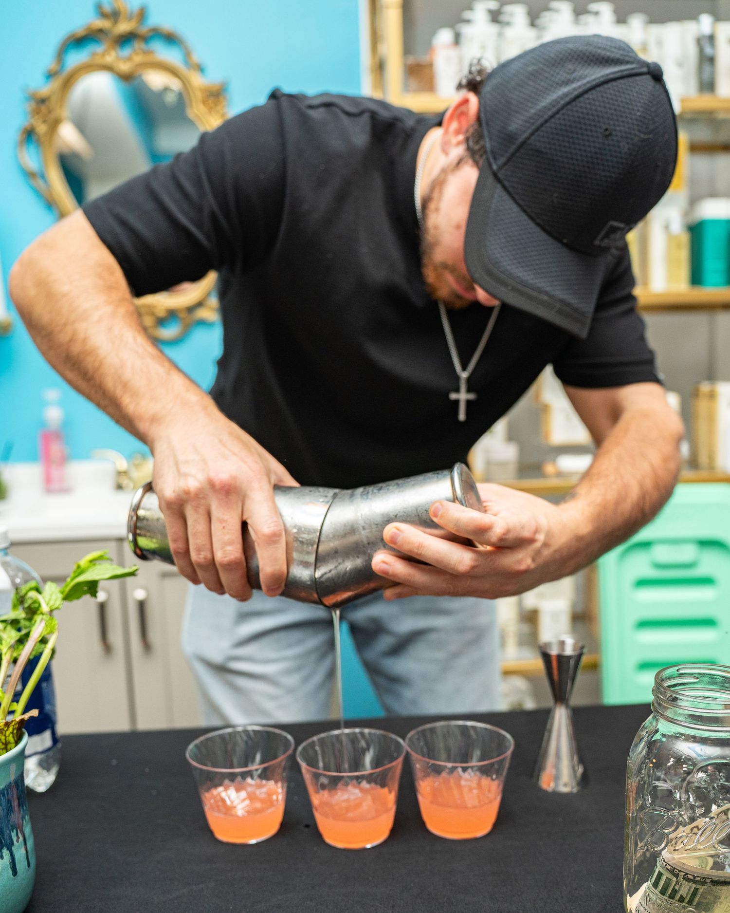 Bartender pouring pink cocktails into glasses using a metal shaker at a stylish bar.