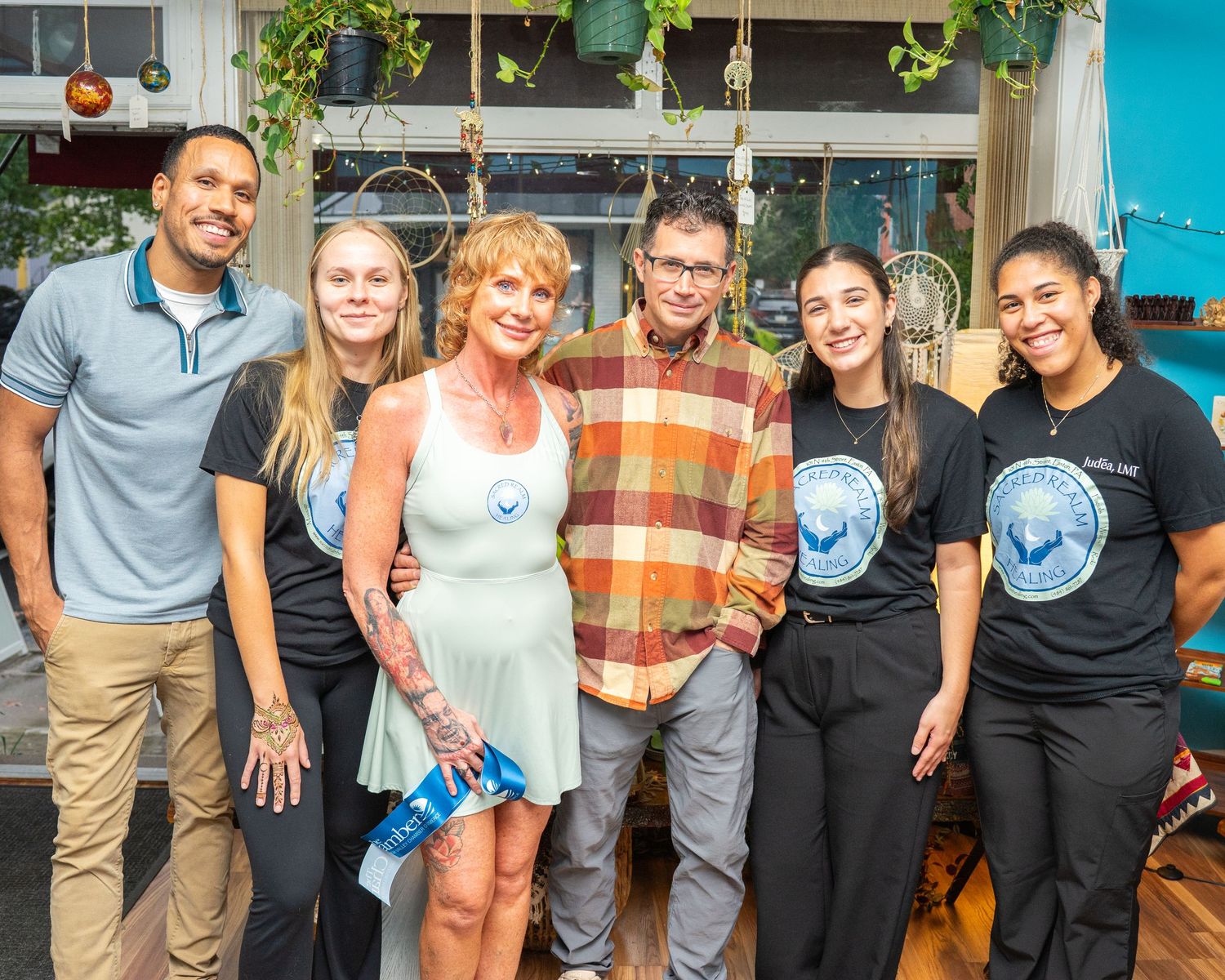 Group of six smiling people posing together indoors at a casual event, wearing matching black shirts and casual attire.