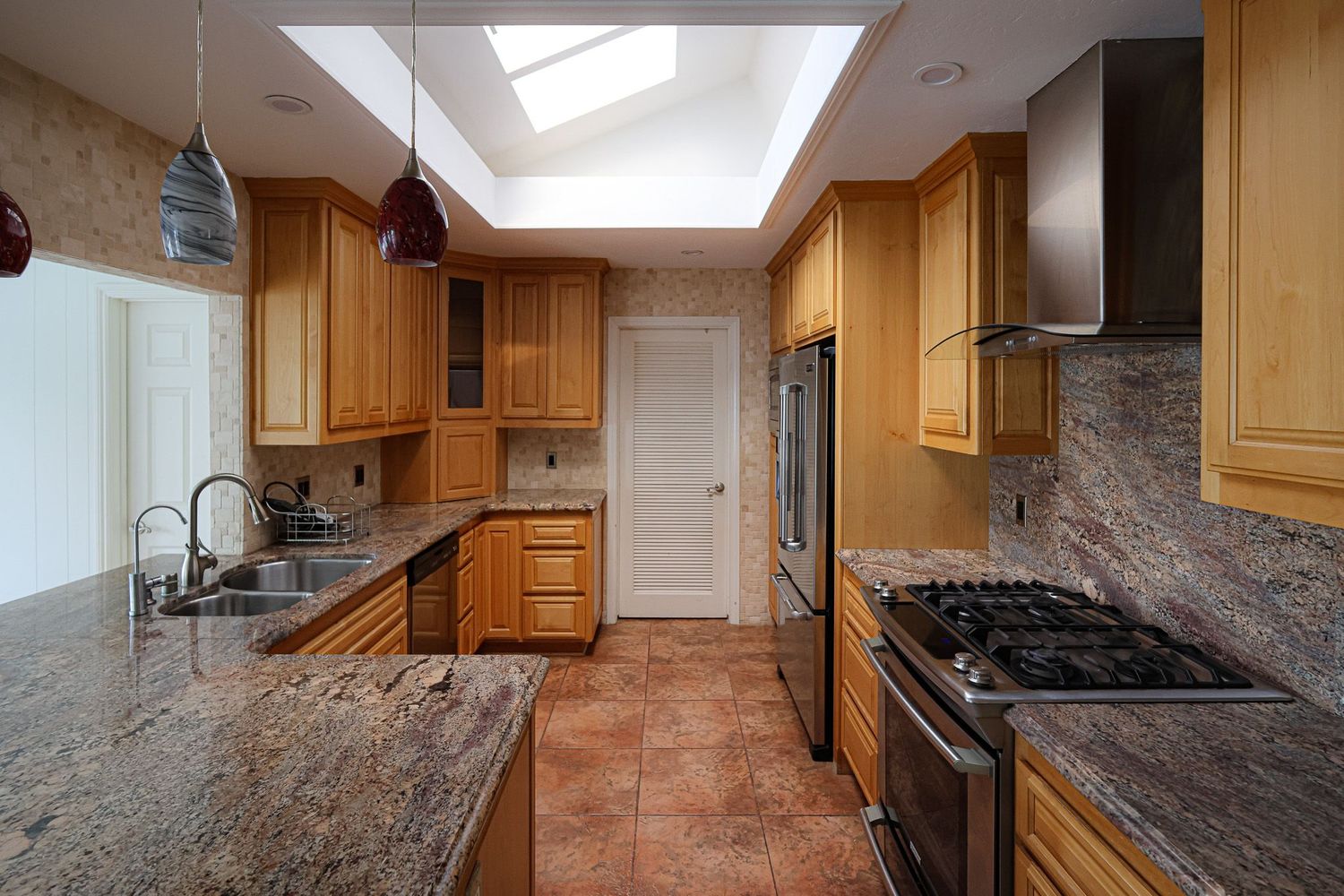 San Diego real estate photography of a modern kitchen with granite countertops, wooden cabinets, a skylight, and stainless steel appliances.