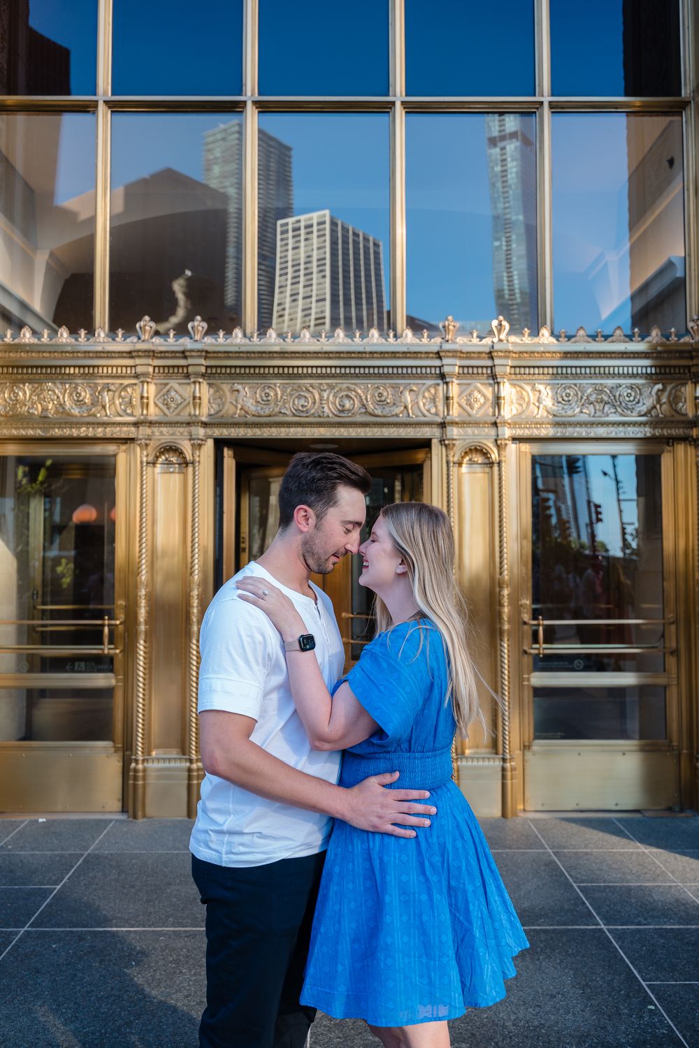 Couple sharing a romantic moment in front of a golden ornate building entrance with city reflections in Chicago.