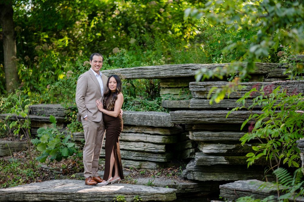 Couple posing on stone steps surrounded by lush greenery in a garden setting.