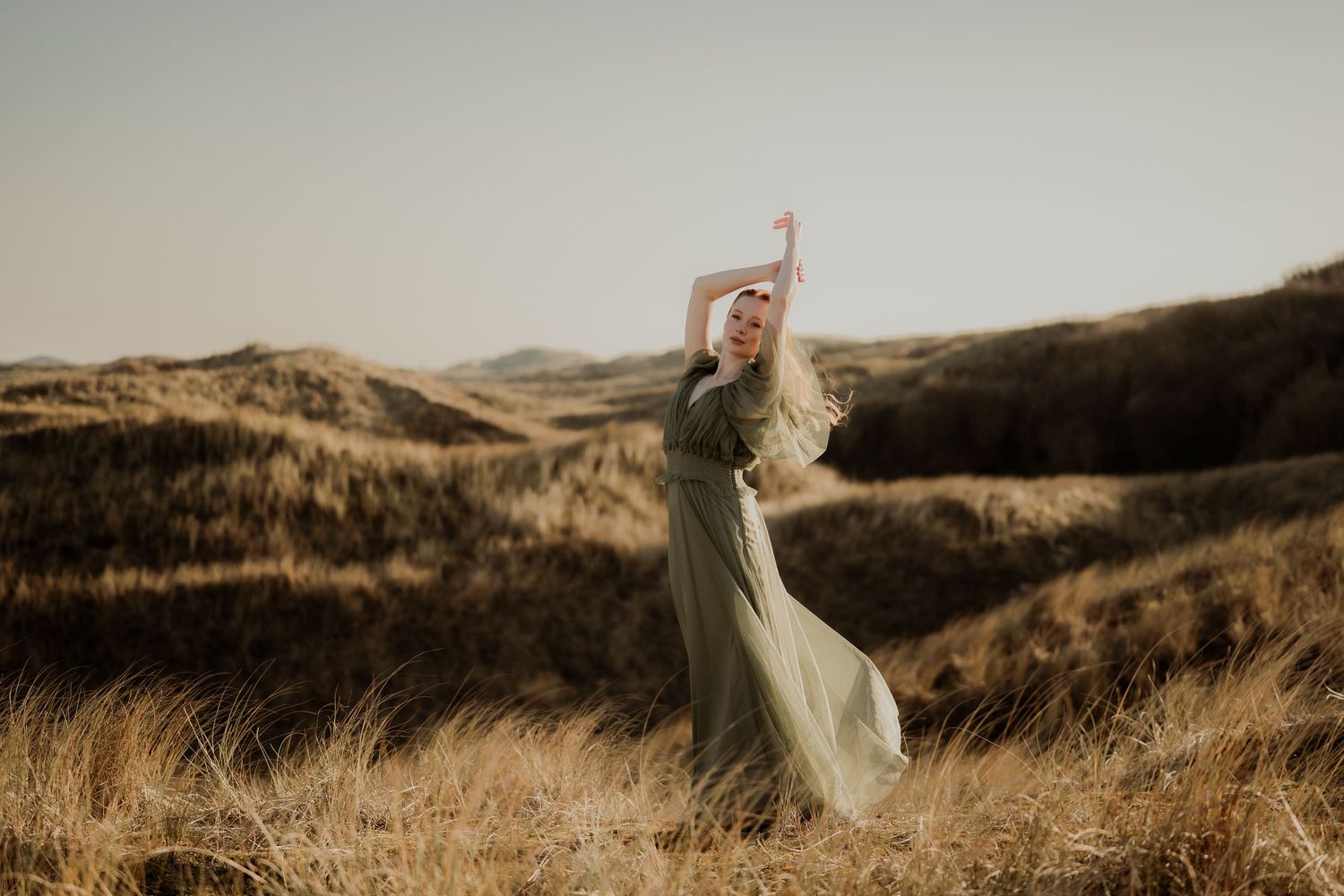 Woman in flowing green dress standing in misty Scottish Highland landscape with mountains in background.