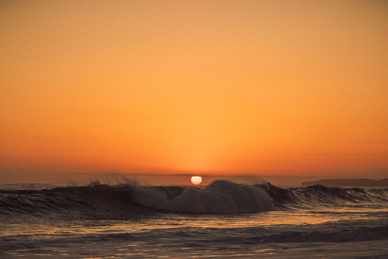 Golden sunset over ocean waves with vibrant orange sky and sun setting on the horizon.