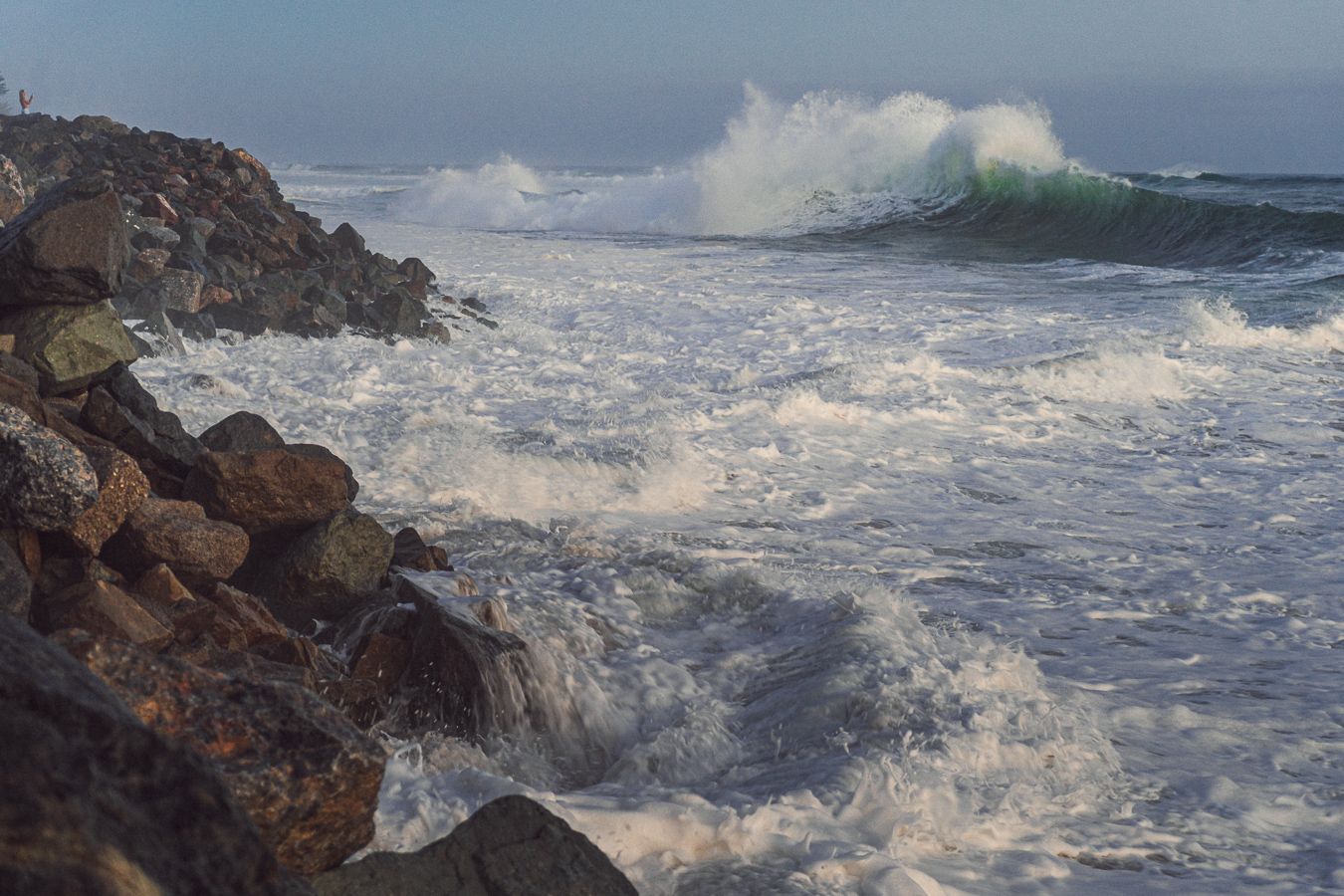 Rough ocean waves crashing against rocky shoreline with white sea foam and spray.
