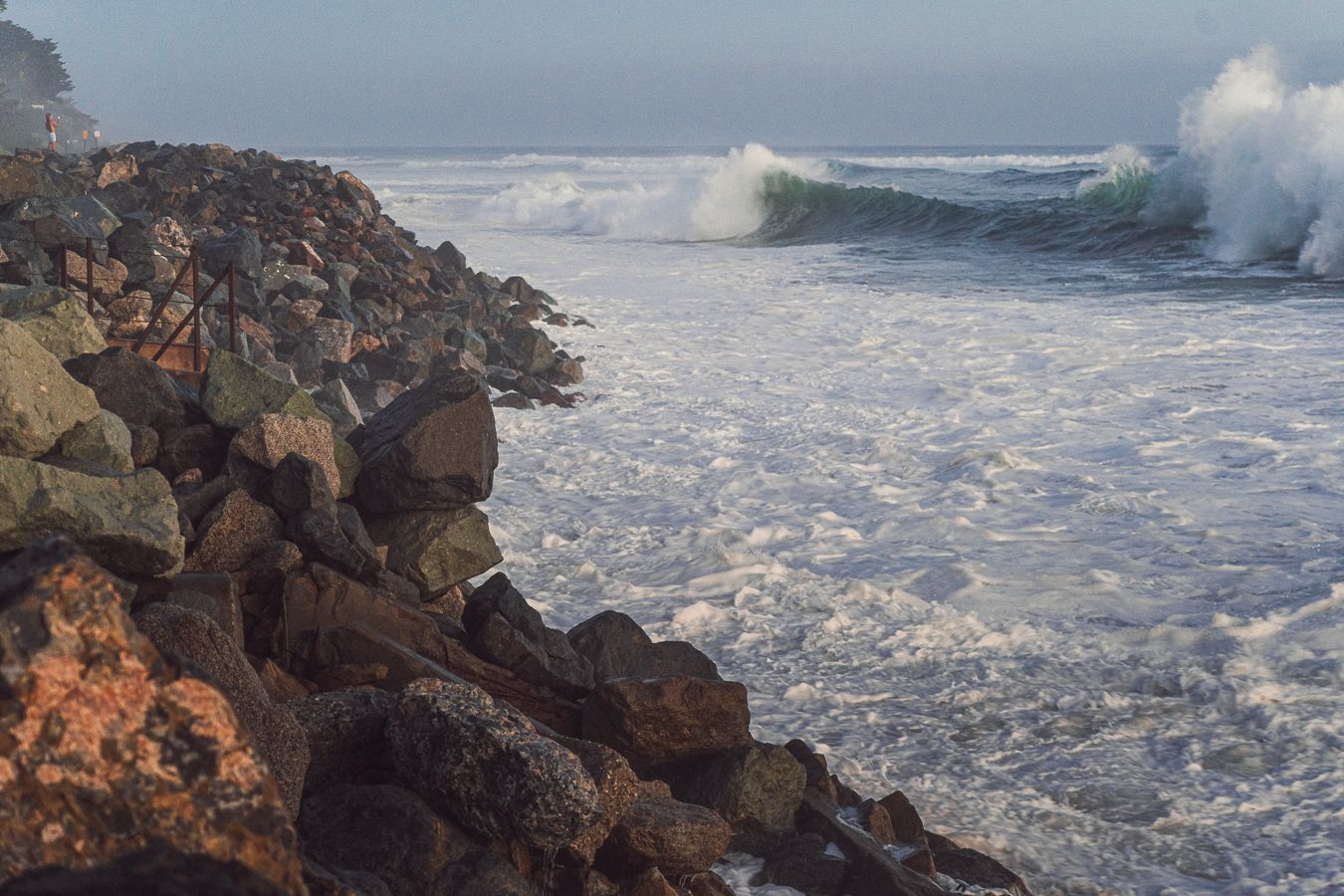 Rocky coastal jetty with turbulent ocean waves crashing along the rugged stone shoreline.
