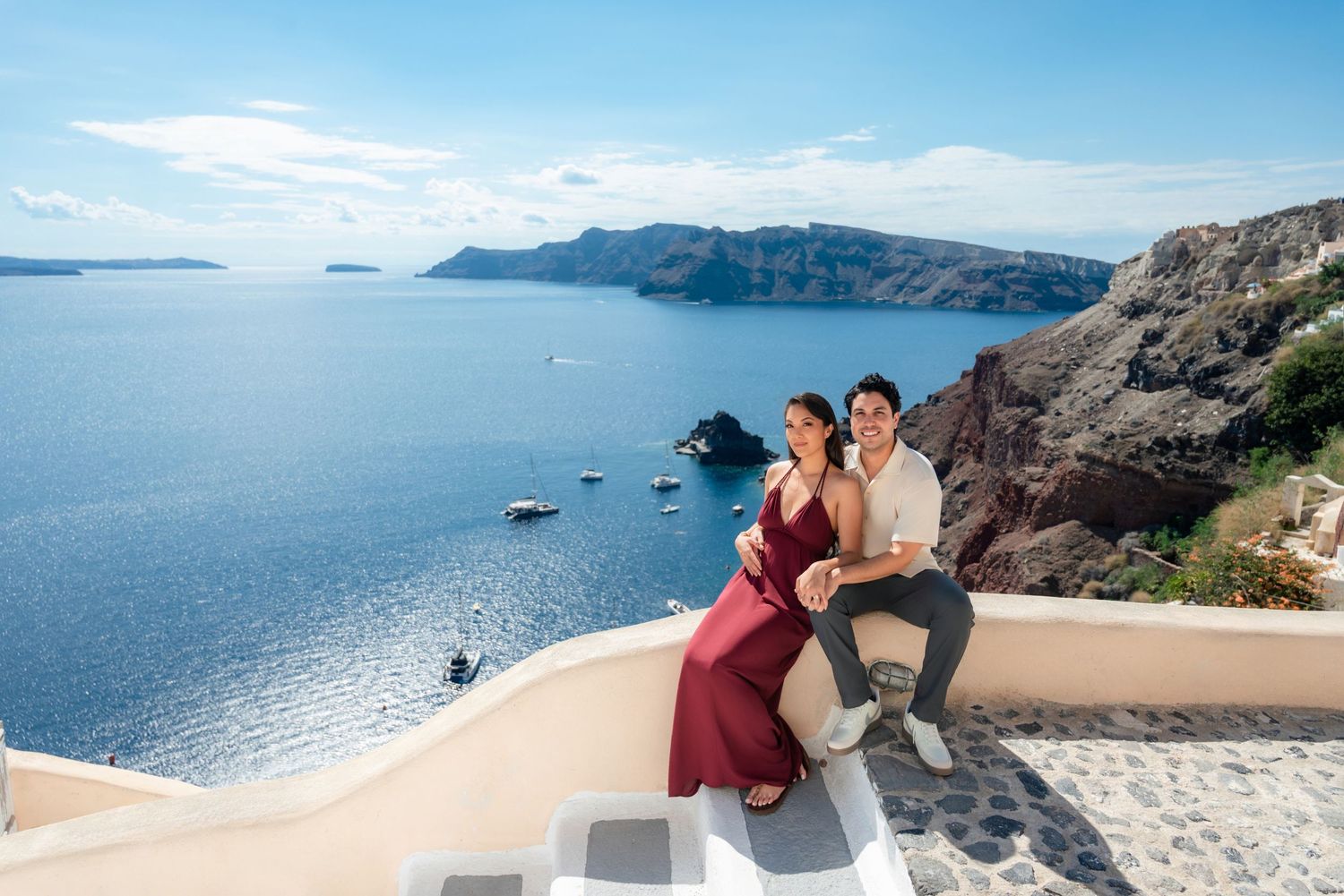 Couple sitting together on white terrace in Santorini Greece with stunning caldera sea views and rocky cliffs.
