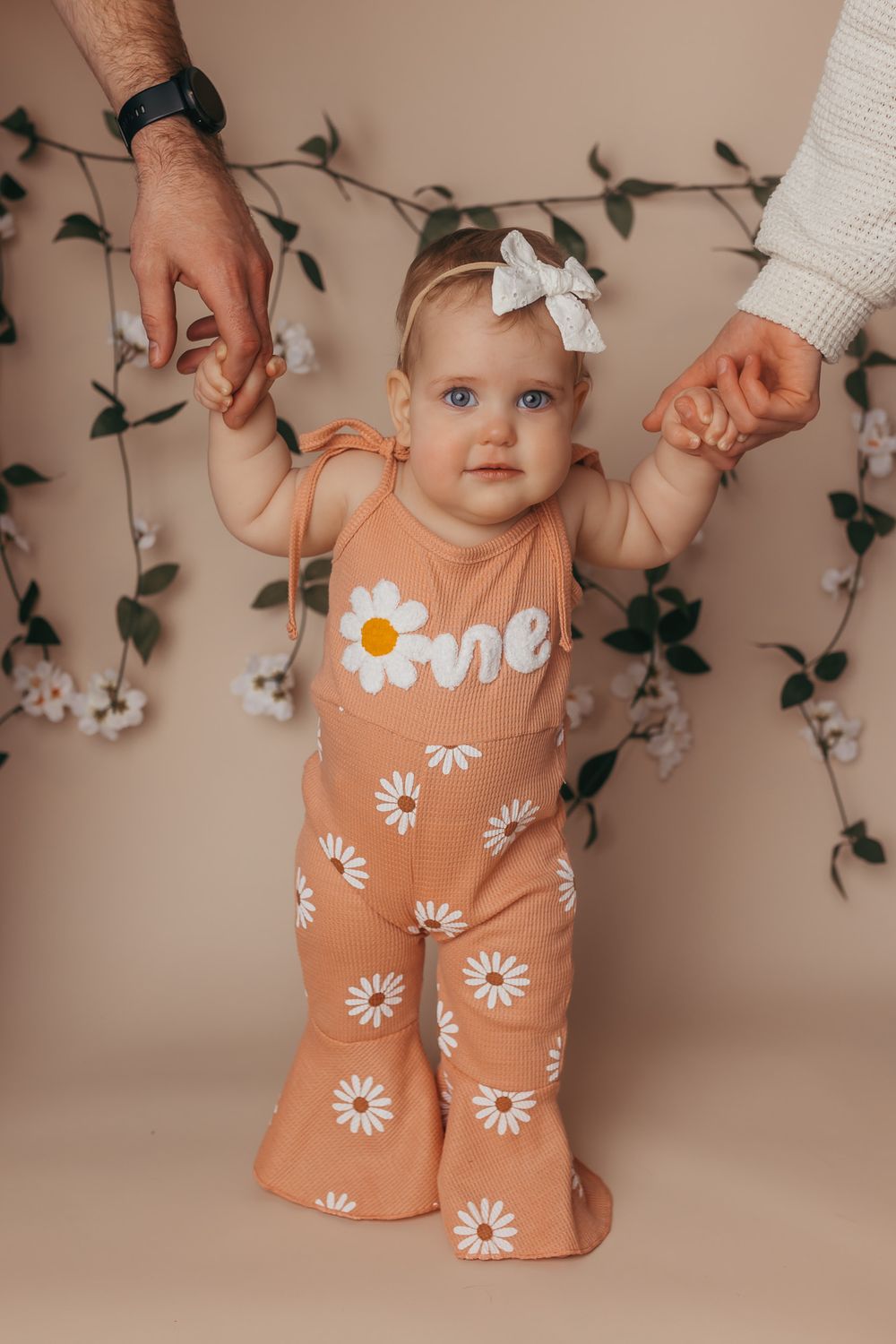 Baby girl hanging on to mom and dads hands while smiling at the camera during her fun one year photography session